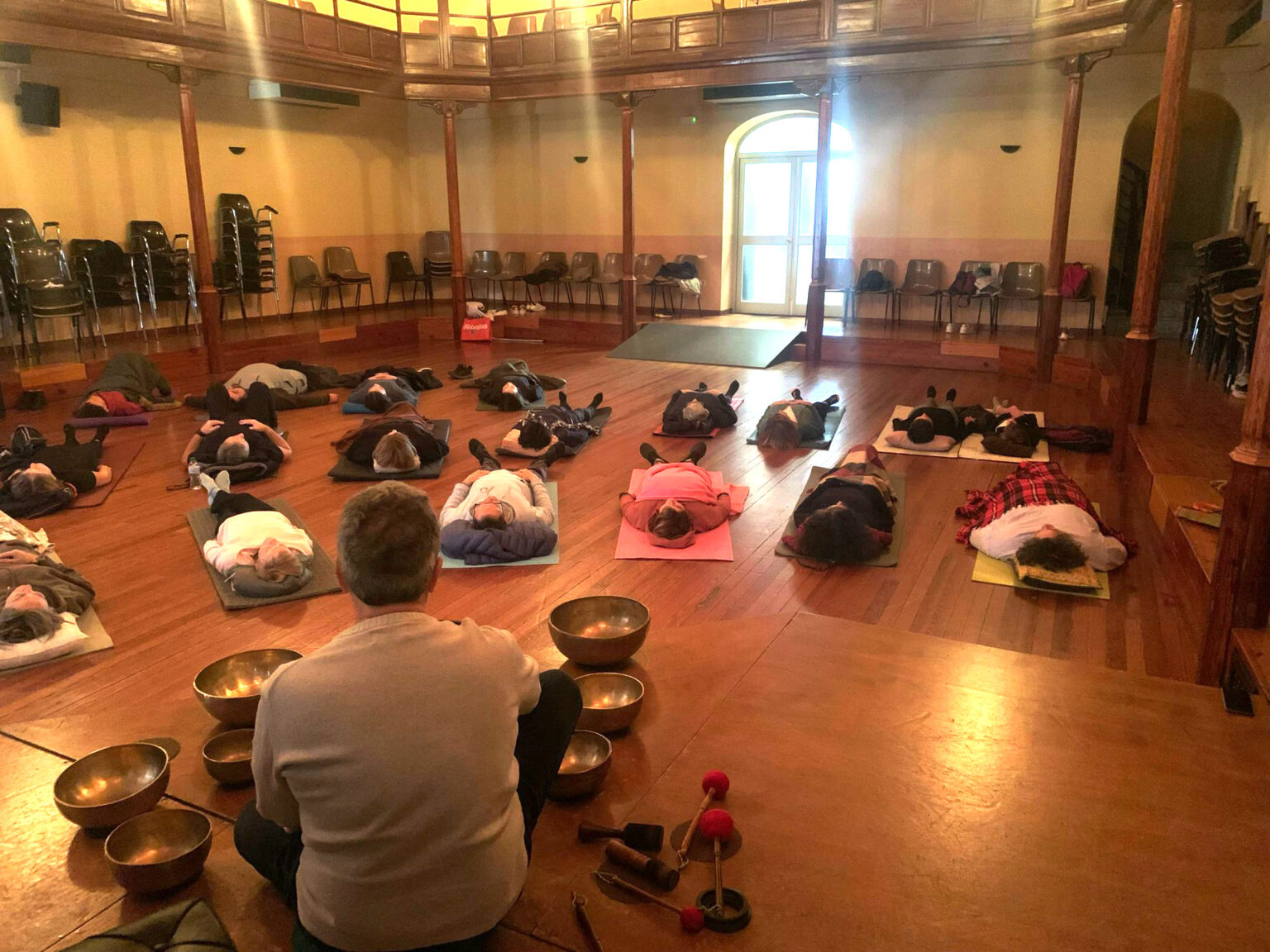 Persones estirades sobre esterilles en una sala amb columnes mentre en Francesc, d'esquena, toca bols tibetans.