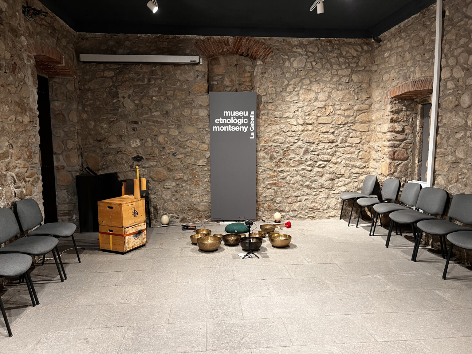 Sala de parets de pedra del Museu Etnològic del Montseny amb cadires en semicercle i bols tibetans a terra, abans del concert.